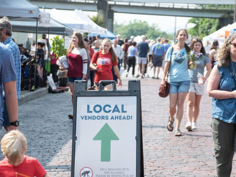 A crowed of people walking on the street at a Farmers Market 