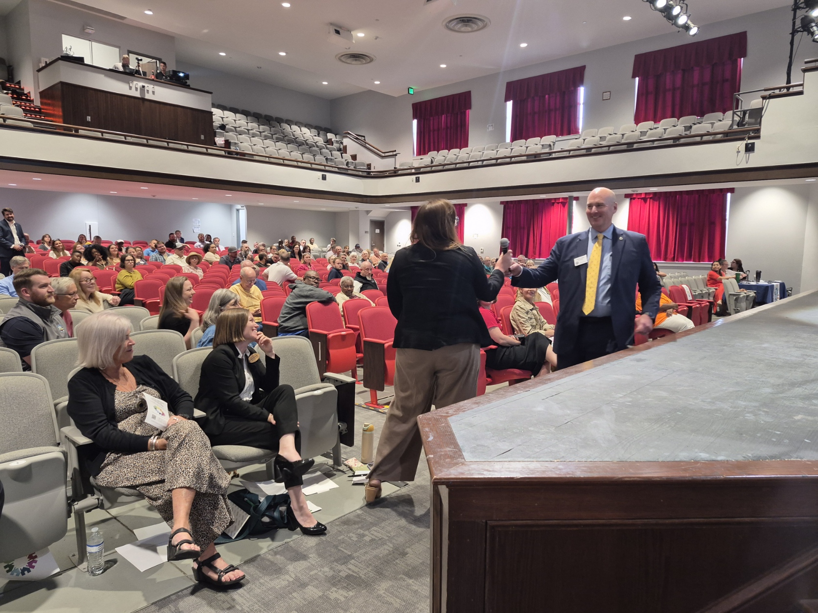 City Manager handing a microphone to a community member in an auditorium