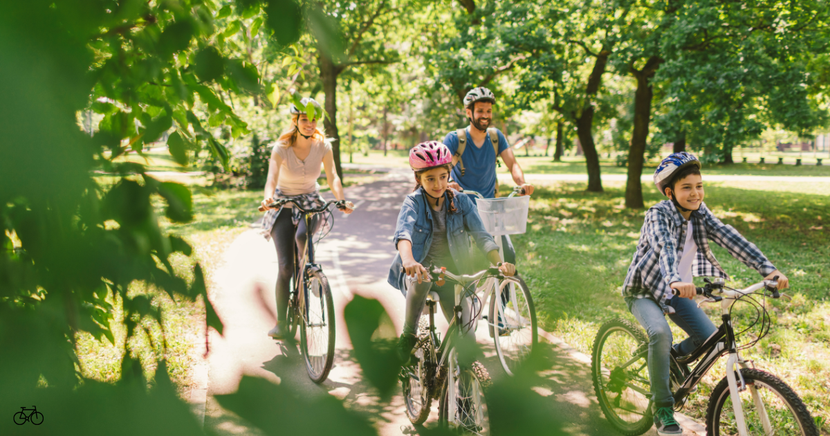 Family of 4 riding bikes in a park wearing bike helments