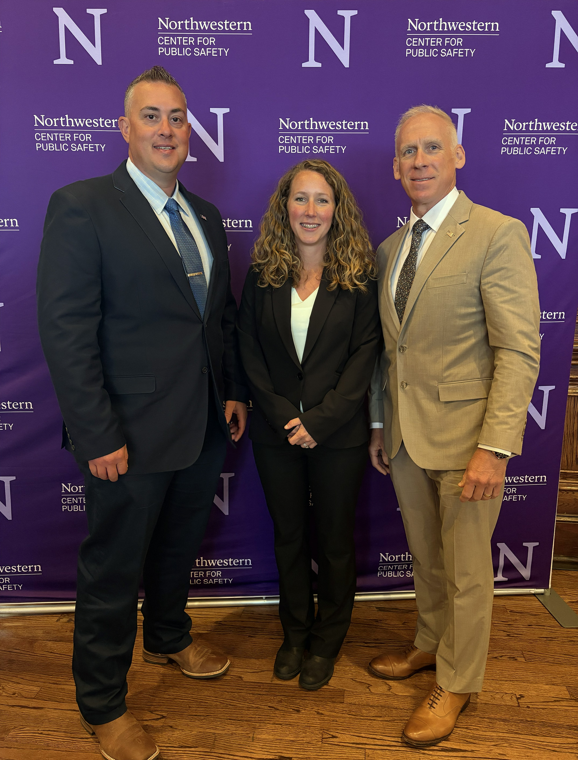 Three people stand in formal attire, smiling, in front of a purple Northwestern University backdrop.
