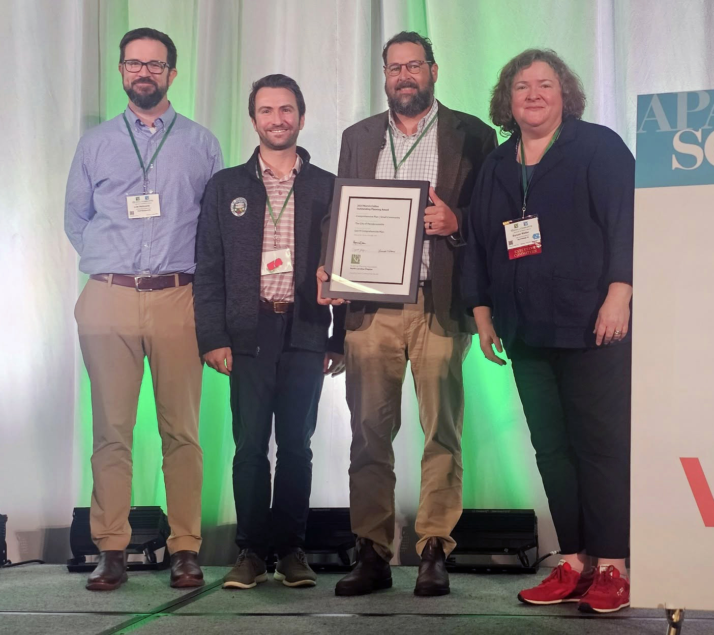 Four people stand and smile, holding an award plaque.