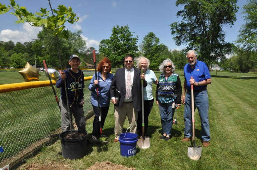 Six individuals stand outside with shovels and trees.